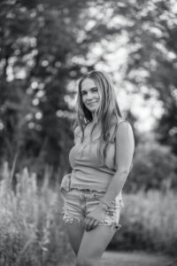 Black and white outdoor portrait of a teen standing in tall grass with soft background blur in Ephrata, PA.