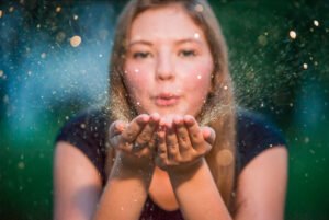 Person blowing golden glitter, magical celebration portrait with warm bokeh.