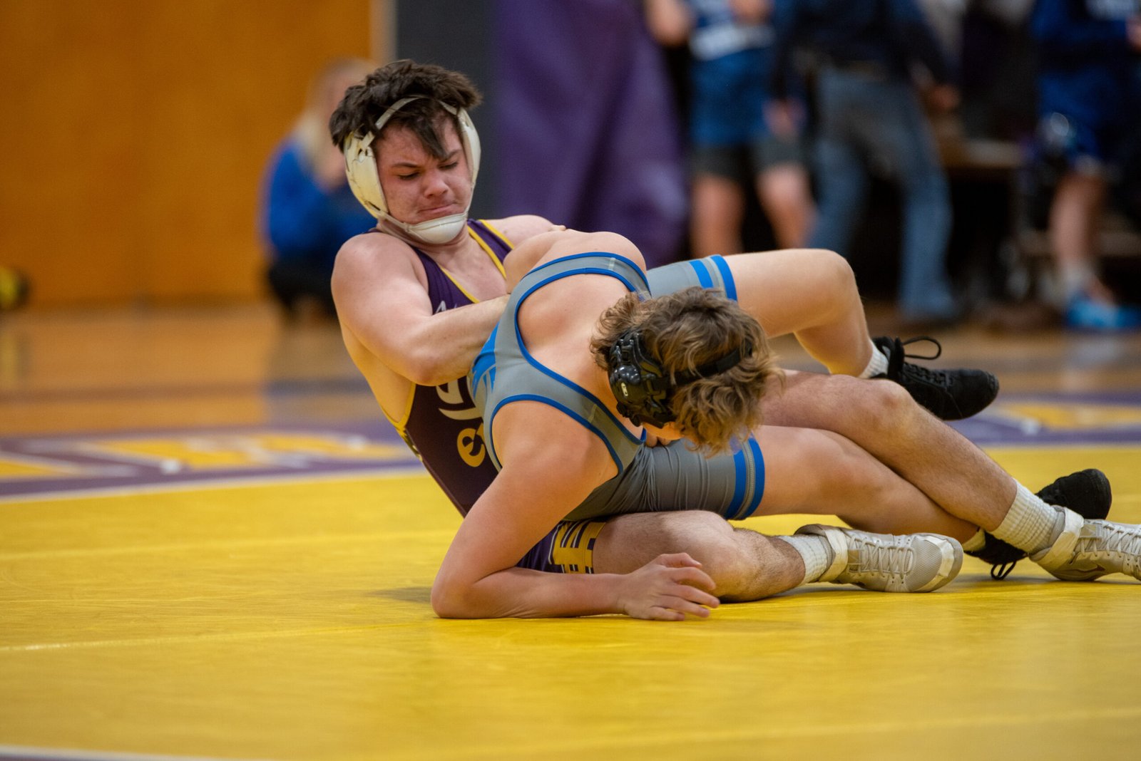 High school wrestlers grapple during an intense match on a yellow mat.