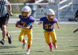Two Ephrata youth football players running downfield carrying a football